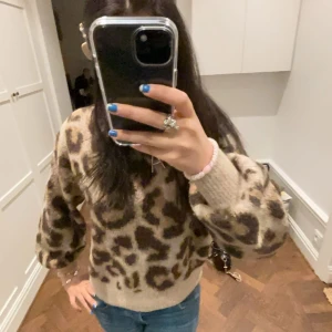 Beige leopardmönstrad stickad tröja - Säljer en cool beige stickad tröja med leopardmönster. Tröjan har långa ärmar och en avslappnad passform, perfekt för en trendig look. Passar bra till jeans eller kjol för en stilren outfit.