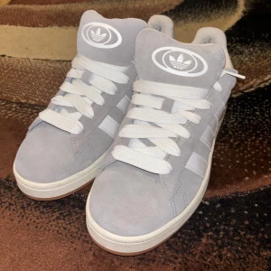 Adiddas Campus gråa  - Snygga grå sneakers från Adidas med vit sula och klassiska tre ränder på sidan. Skorna har en rund tå och snörning framtill. Perfekta för en avslappnad stil. Har bara används vid ett tillfälle. Pris kan diskuteras!