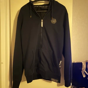 Svart hoodie från Philipp Plein - Snygg svart hoodie från Philipp Plein med dragkedja och huva. Logga på bröstet och luvan.
