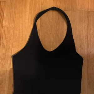 Svart halternecklinne från H&M stl M - Säljer ett stilrent svart halternecklinne från H&M:s Divided-kollektion. Perfekt för en trendig look, med en enkel design som passar till många olika outfits. Linnet är tillverkat i ett mjukt och bekvämt material.