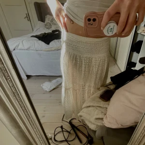 Vit långkjol med spetsdetaljer - Säljer en vacker vit långkjol med fina spetsdetaljer. Kjolen har en luftig och bekväm passform, perfekt för varma dagar. Den är elegant och kan enkelt matchas med olika toppar. Perfekt för en somrig look! 