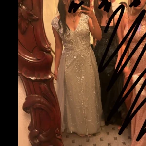 Silverfärgad balklänning - Elegant silverfärgad klänning som jag hade på balen, med v-ringning och detaljerade glittriga stenpaljeter . Klänningen har en öppen rygg och är ärmlös, vilket ger en sofistikerad look. Perfekt för balen eller en fest! Jag köpte den i somras för 4500kr men jag är villig att diskutera om pris. 