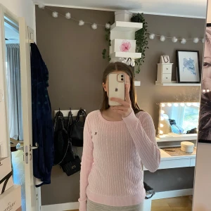 Rosa stickad tröja från Gant - Säljer en söt rosa stickad tröja från Gant med kabelstickat mönster. Tröjan har långa ärmar och en liten logga på bröstet. Perfekt för en mysig dag!