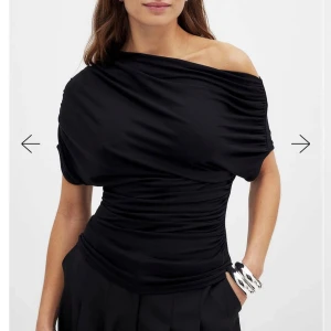 Svart offshoulder soft line draperad topp - Elegant svart offshoulder topp med draperad design och korta ärmar från NA-KD. Perfekt för fest, har klippt bort lappen i ryggen men annars är den som ny🫶