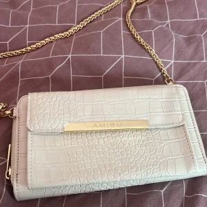 Vit axelväska från Amisu - Snygg vit axelväska från Amisu med krokodilpräglat mönster och guldfärgad kedja. Perfekt för att ge en touch av elegans till din outfit. Väskan har en praktisk dragkedja och en stilren design.