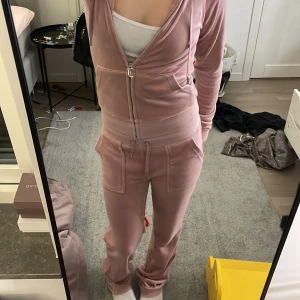 Rosa velour hoodie från Juicy Couture - Säljer ett jätte fint Juicy Couture sätt. Som är lite smutsig på armarna som man ser på bilden men verkligen inget man tänker på när man har på sig. Sen är också den saken som sitter vid luvan av men den är superlätt att sy fast (Har gjort det på min kofta jag har). Det är också en grön liten fläck nere på baksidan av benet nära fotleden det ser man absolut inte tydligt på. Sen är silver detaljerna på byxsnörerna lite rostiga och lösa men lätt att fixa med lim (har gjort det på mina andra byxor)