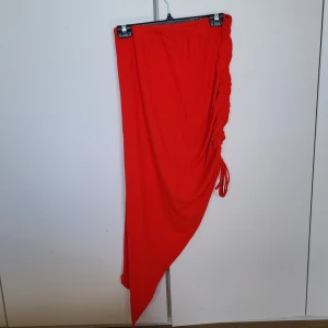 Röd asymmetrisk kjol från Shein - Snygg röd asymmetrisk kjol från Shein med ribbad textur och snörningsdetalj på sidan. Perfekt för att sticka ut med en unik stil. Kjolen har en modern design som ger en cool look.