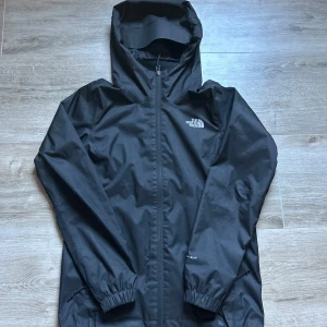 Svart regnjacka från The North Face - Säljer en svart regnjacka från The North Face med huva och dragkedja. Jackan har långa ärmar och elastiska muddar. Perfekt för regniga dagar och utomhusaktiviteter. Storleken är s för kvinnor men passar även för män som har xs