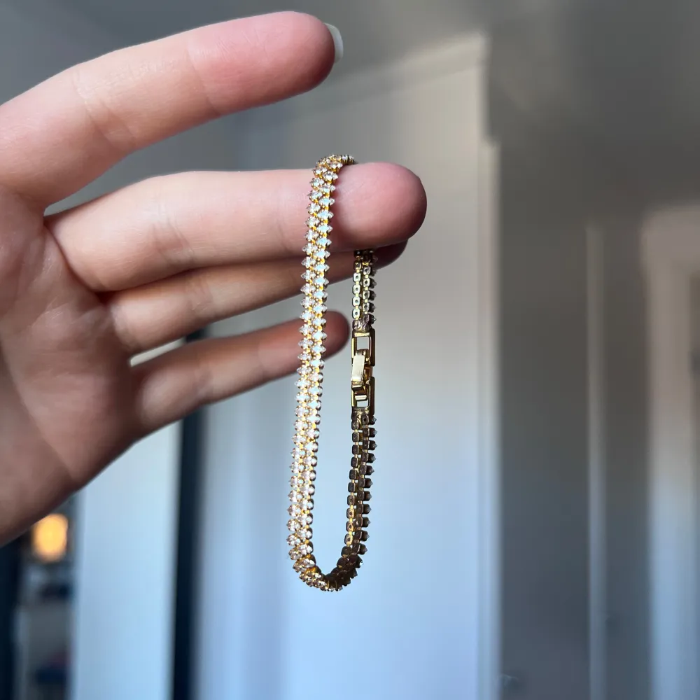 Elegant guldarmband prytt med glittriga stenar. Perfekt för att ge en touch av glamour till din outfit. Armbandet har en säker låsning och en klassisk design som passar till många tillfällen. Har blivit lite mörkt på insidan - se sista bilden! Önskar du veta exakta mått? Tveka inte att höra av dig!. Asusteet.