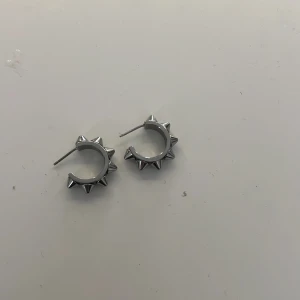 Silvriga örhängen med nitar - Snygga silvriga örhängen i form av ringar med spetsiga nitar runtom. Perfekta för att ge en edgy touch till din stil. Lätta att bära och passar till många olika outfits.