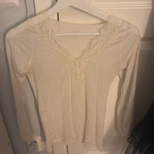 Vit långärmad topp med spetsdetaljer -  vit långärmad topp från Intimissimi med v-ringning och spetsdetalj runt halsen.