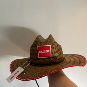 Stråhatt Full Send *HELT NY* - Snygg brun cowboyhatt med röd kant och Full Send-logga framtill. Perfekt för att sticka ut på nästa event. Hatten har en flätad design som ger en autentisk känsla.