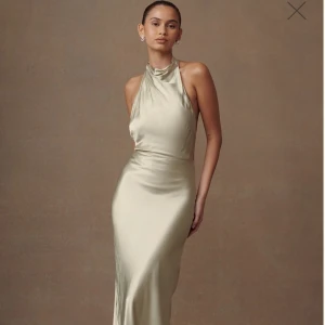 Champagnefärgad (sage) långklänning från Meshki - Elegant champagnefärgad långklänning i satin från Meshki. Klänningen har en halterneck-design med öppen rygg och knappar längs ryggen. Perfekt för bal eller finare tillställningar. Beställde hem flera balklänningar så är tvungen att sälja vidare några, lappar och allt är kvar, endast provats! 