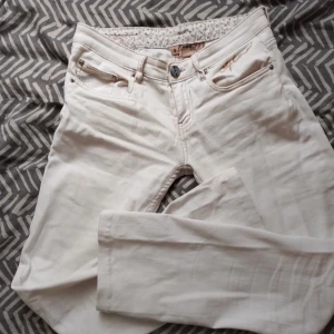 Vita lågmidjade jeans - Snygga vita lågmidjade jeans med broderad textdetalj vid fickan. Byxorna har en knapp och dragkedja framtill samt två bakfickor med dekorativa sömmar. Perfekta nu inför våren och sommaren. Står strl S men jag skulle säga att de är mer som XS i storleken!