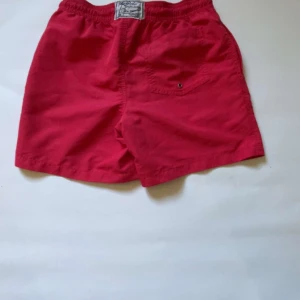 Röda shorts  - Snygga röda shorts med elastisk midja och snörning framtill. Perfekta för sommarens alla äventyr. En liten broderad logga på framsidan ger en extra touch. Inte använda