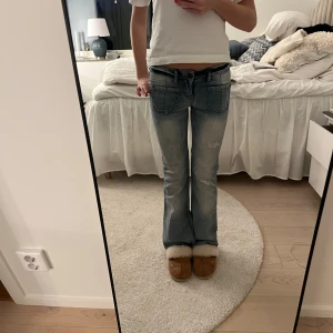 Blå lågmidjade bootcut jeans - Snygga blå bootcut jeans med slitna detaljer och stora framfickor. Perfekta för en avslappnad stil. De har en klassisk femficksdesign och en knappgylf. Älskar!! Midjemått: ca 36 Cm rakt över , innerbenslängd: ca 74cm🥹🥹🌸😇🌸🌸🥹 stretchiga 