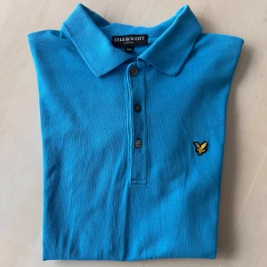 Blå pikétröja från Lyle & Scott - Säljer en blå - nästan åt det turkosa hållet - pikétröja från Lyle & Scott. Det är en mycket vanlig tröja, vanlig krage och knappar samt  loggan på bröstet. 