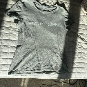 Grå t-shirt från Calvin Klein - Säljer en stilren grå t-shirt från Calvin Klein Jeans. T-shirten är tillverkad i 100% bomull och har korta ärmar. Perfekt för en avslappnad look.