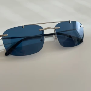 Blå Eytys Avery solglasögon - Säljer ett par helt nya och oanvända Eytys Avery solglasögon. De har en cool och unik design med rektangulära glas och en minimalistisk metallram som ger en modern look  Originalpris 1100kr
