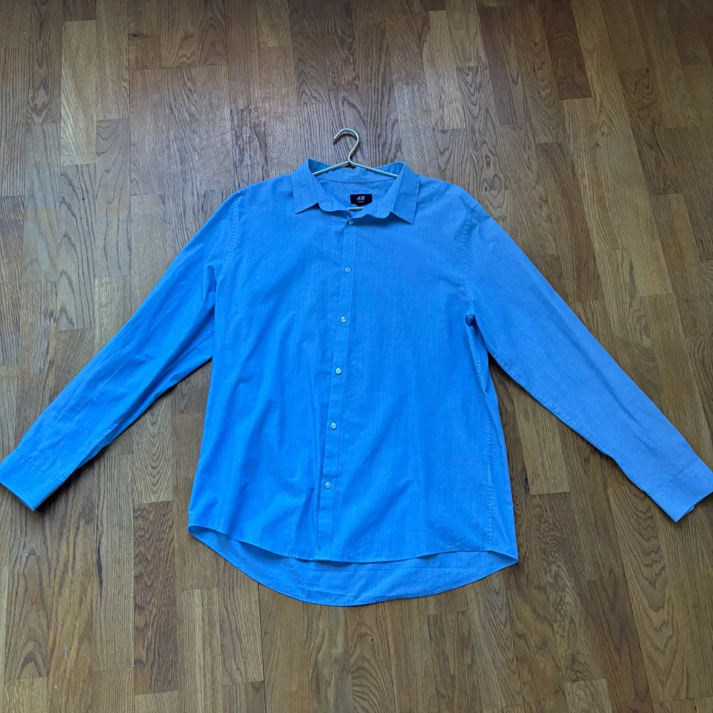 Snygg blå långärmad skjorta med klassisk krage och knappar framtill. Perfekt för en stilren look. Skjortan har en normal passform och är tillverkad i ett lätt och bekvämt material.. Paidat.