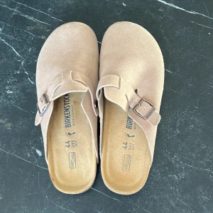 Beige mocka sandaler från Birkenstock - Säljer ett par bekväma beige sandaler från Birkenstock i mocka. De har en justerbar rem med spänne och en ergonomisk fotbädd för extra komfort. Perfekta för avslappnade dagar. Säljer då de är för små, helt oanvända.