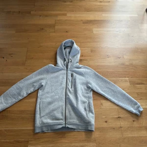 Grå hoodie från Sail Racing (pris kan diskuteras) - Säljer en stilren grå hoodie från Sail Racing med dragkedja och en praktisk bröstficka. Perfekt för kyliga dagar med sin mjuka insida och justerbara huva. Den har en broderad logga på bröstet och ribbade muddar för extra komfort. Storlek 150 och köpt från kidsbrandstore för 1000. Ett liten skavank vid armbågen så därför 600 kr rabatt.