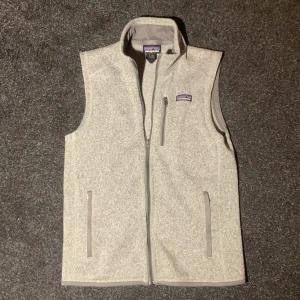 Grå Patagonia väst - Grå fleeceväst från Patagonia. Västen har tre fickor med dragkedja med en stilren och enkel design. Perfekt för lager-på-lager och soft-vibes.