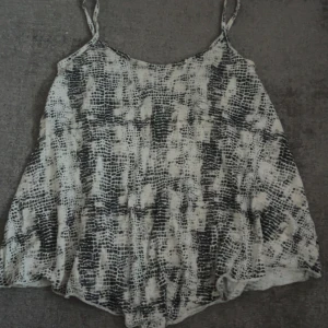 Svartvit linne från Gina Tricot - Säljer ett luftigt linne från Gina Tricot i storlek S. Toppen har smala axelband och ett svartvitt mönster som påminner om ormskinn. Perfekt för varma dagar och enkel att styla med jeans eller shorts. Säljer pågrund av att jag inte använder den.