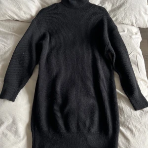 Svart stickad poloklänning - Mysig svart stickad klänning med polokrage och långa ärmar. Modellen är rak och enkel, perfekt för lager-på-lager och en chill vibe. Ribbstickat material som ger en snygg struktur och extra värme under kyliga dagar.