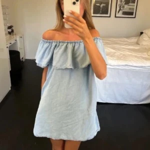Ljusblå offshoulder klänning - Superfin ljusblå kortklänning i offshoulder-modell med volang upptill. Klänningen är i mjukt bomullsliknande tyg och har en avslappnad passform. Perfekt för varma dagar när du vill ha en chill och trendig look.