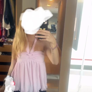 Ljusrosa omlott halterneck topp - Supersöt ljusrosa halterneck topp med omlottdetalj och plisserad nederdel. Toppen är ärmlös och har en flowy passform som ger en romantisk vibe. Perfekt för varma dagar eller när du vill känna dig extra fin. Från Gina Tricot 14+