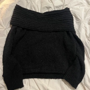 Svart offshoulder stickad tröja Boohoo - Mysig svart stickad tröja från Boohoo med bred ribbad offshoulder-krage. Tröjan har lång ärm och en loose fit som ger en chill vibe. Perfekt för lager på lager under höst och vinter. Superenkel att styla med jeans eller kjol.