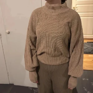 Beige stickad polotröja - Säljer en beige stickad polotröja med ribbad struktur och långa ärmar. Tröjan har en loose passform och hög krage som ger en chill och avslappnad vibe. Perfekt för lager-på-lager under hösten och vintern.