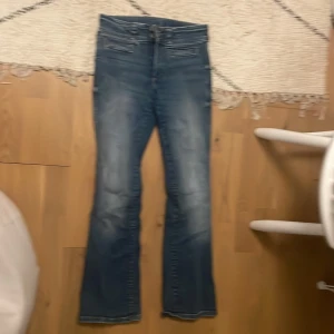 Blå bootcut jeans med fickdetaljer - Snygga blå jeans med bootcut-modell och markerade fickor både fram och bak. Jeansen har dubbla knappar i midjan och klassiska bälteshällor. Bakfickorna har lock och silverfärgade knappar. Perfekta för dig som gillar en retroinspirerad look. Inga slitningar, då jag knappt använt de!