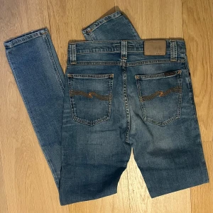 Nudie Jeans High Kai ljusblå jeans - Säljer ett par Nudie Jeans High Kai i ljusblå tvätt med klassiska orange sömmar och snygga detaljer på bakfickorna. Jeansen är tillverkade i 98% bomull och 2% elastan för en bekväm stretchig känsla. Modellen har smal passform och normal midja. Inga som helst defekter tveka inte att fråga!