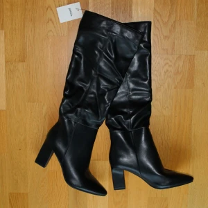 Svarta stövlar med klack - Snygga svarta stövlar från Pimkie i skinnimitation med hög klack och spetsig tå. Knähöga och enkla att matcha med en kjol, klänning eller jeans för en höstig look. Har aldrig blivit använda. Köpta här på plick för 350 kr, säljes nu för 200 kr då de inte passar mig.