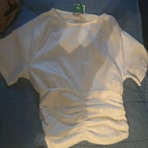 Vit blus med rynk från Anna Field - Säljer en stilren vit blus från Anna Field med korta ärmar och snygg rynkdetalj i midjan. Blusen har rund halsringning och är tillverkad i ett mjukt, lätt material som ger en fräsch look. Perfekt för dig som gillar enkel men trendig stil. Aldrig använd ! Lappen är fortfarande på också 