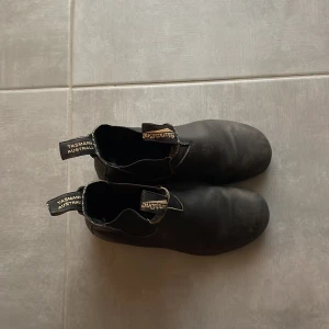 Svarta Blundstone chelsea boots i skinn - Klassiska svarta chelsea boots från Blundstone i robust, vattenavvisande skinn med elastiska paneler på sidorna och grov sula för extra grepp. Perfekta för dig som vill ha en tidlös och stilren look med australiensisk känsla. Dragflikar med logga för enkel påtagning. Perfekta nu i höst och vinter. 