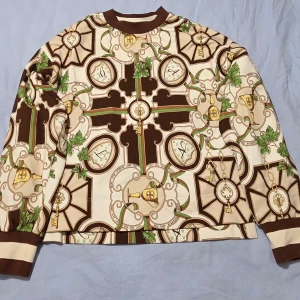 Oanvänd mönstrad långärmad tröja från Gant, S - Säljer en unik långärmad tröja från Gant med brunt, beige och grönt mönster av nycklar, kalkar och blad. Tröjan har rund halsringning och muddar i brunt. Perfekt för dig som vill sticka ut med en cool och detaljerad design.