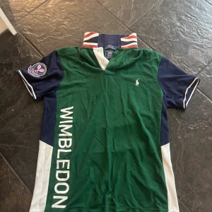 Äkta Polo Ralph Lauren unik pikétröja Wimbledon - Snygg Wimbledon-inspirerad pikétröja från Polo Ralph Lauren i grönt, blått och vitt. Tröjan har klassisk krage med brittisk flagga på insidan, korta ärmar och Wimbledon-logga på ärmen. Perfekt för dig som gillar exklusiva och unika plagg! Jag har supermånga bilder så bara skriv om ni villa ha fler, ha mått eller har andra frågor! Jag svarar snabbt⭐️