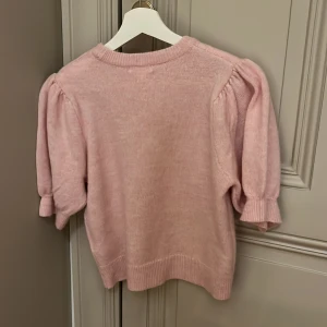 Ljusrosa stickad tröja Gina Tricot - Supersöt ljusrosa stickad tröja från Gina Tricot med puffiga korta ärmar och ribbade muddar. Perfekt för dig som gillar en feminin och trendig look. Mjuk och skön, passar till både jeans och kjol. Använd max 3 ggr