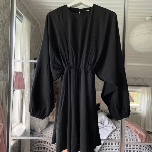 Svart klänning med vida ärmar - Svart klänning från bikbok med markerad midja och vida, långa ärmar. Klänningen har en enkel rund halsringning och slutar ovanför knäna. 