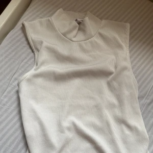 Vit ribbad polotopp från Amisu - Säljer en stilren vit polotopp från Amisu i storlek S. Toppen är ribbad och ärmlös med hög krage som ger en clean och modern vibe. Perfekt att styla med jeans eller kjol för en fräsch look. Materialet känns mjukt och följsamt mot huden.