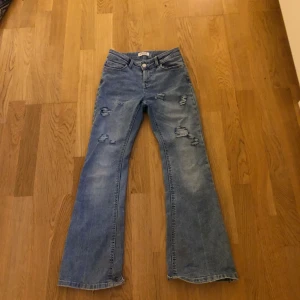 Blå bootcut jeans från Lindex 152 - Snygga blå bootcut jeans från Lindex med slitna detaljer och har hål under fickan och lite slitna längst ner. De är mid waist.