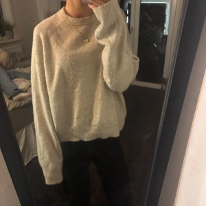 Beige stickad tröja  - Mysig beige stickad tröja med avslappnad passform och långa ärmar. Tröjan har ribbade muddar vid ärmslut och nederkant, perfekt för lager på lager under kyliga dagar. Enkel och stilren design som passar till allt.