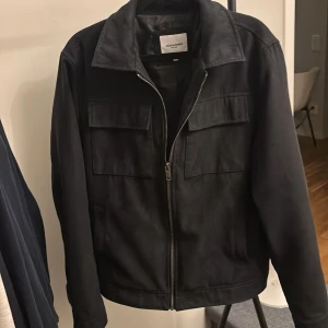 Mörkblå Overshirt - Säljer en mörkblå jacka från Jack & Jones i storlek S. Jackan har två stora bröstfickor med lock, klassisk krage och hel dragkedja framtill. Perfekt för dig som gillar en stilren och enkel look. Inga defekter! Väldigt bra skick!