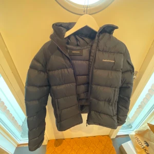 Mörkblå pufferjacka Peak Performance - Säljer min mörkblå pufferjacka från Peak Performance. Jackan har en schysst quiltad look, huva och dragkedja framtill. Perfekt för dig som vill ha en varm och snygg jacka med clean stil och sköna fickor. Passar dig som gillar loose fit och vill ha något som funkar hela vintern.