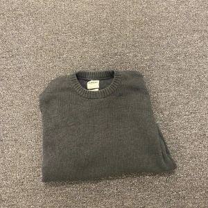 Mörkgrå stickad tröja från Dobber - En stilren mörkgrå stickad tröja från Dobber i storlek medium. Tröjan har rund halsringning, ribbade muddar vid ärmslut och nederkant samt lång ärm. Perfekt för lager-på-lager och enkel att matcha med jeans eller chinos.
