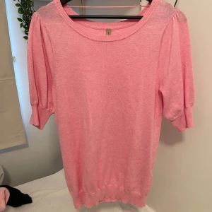 Rosa stickad topp med puffärm - Supersöt ljusrosa stickad topp med puffiga kortärmar och rund halsringning. Mjuk och skön, perfekt för vår och sommar. Ribbad kant vid ärmslut och nederkant ger en snygg passform. 