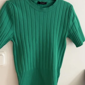 Grön ribbad stickad tröja  - Snygg grön stickad tröja med ribbad struktur och korta ärmar. Perfekt till vår och sommar, enkel att matcha med både jeans och kjol. Rund halsringning och figurnära passform ger en fräsch look.